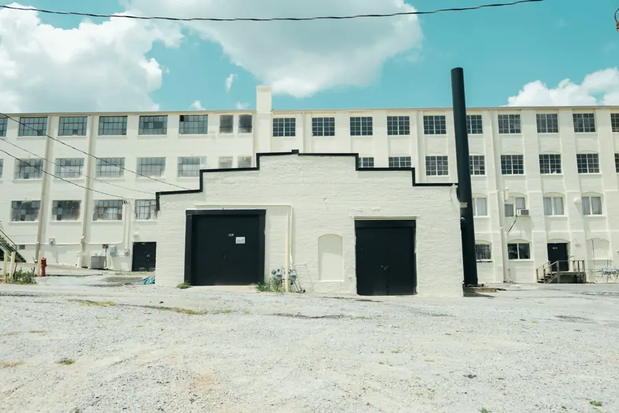 A cream brick flex building with two large roll-up doors, in front of a longer four-story brick industrial block.