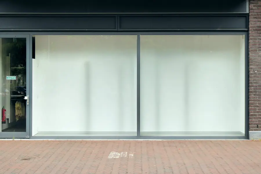 An empty ground-floor storefront with two large glass panes, a glass entry door and a brick-paved sidewalk.