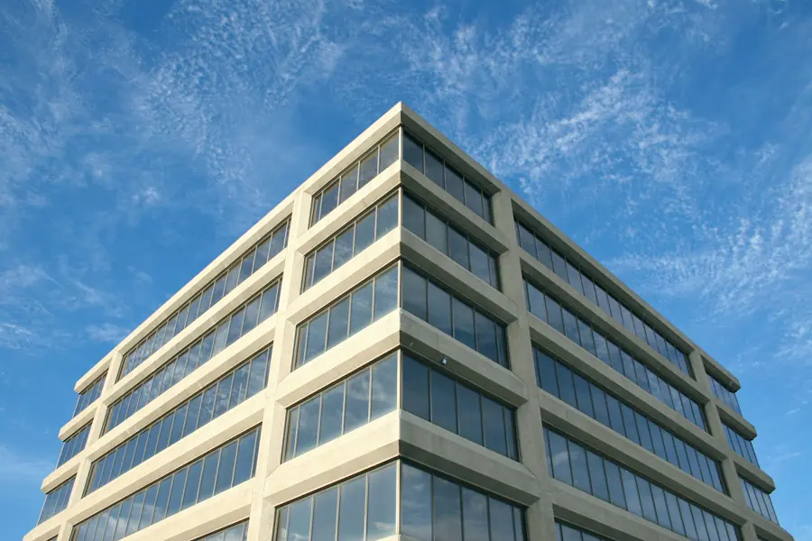 The corner of a six-story office building with pale stone bands and long ribbon windows against a blue sky.