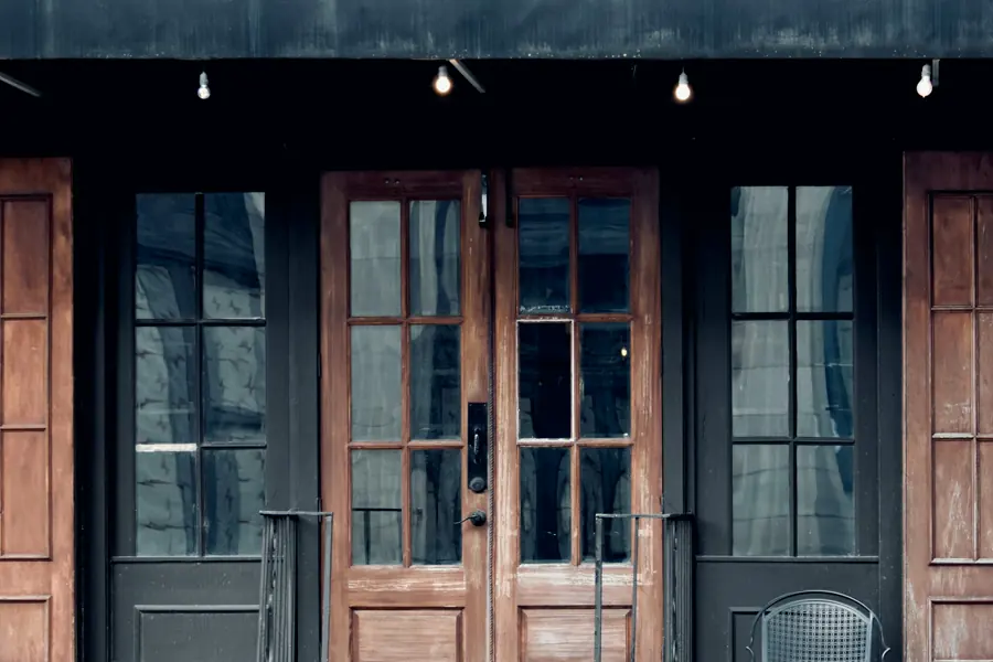A one-story retail front with wooden double doors, tall glass side panels and a dark metal awning over the walk.