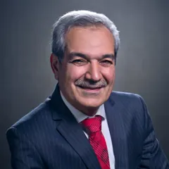 A smiling older man with grey hair and a moustache in a navy suit and red tie.