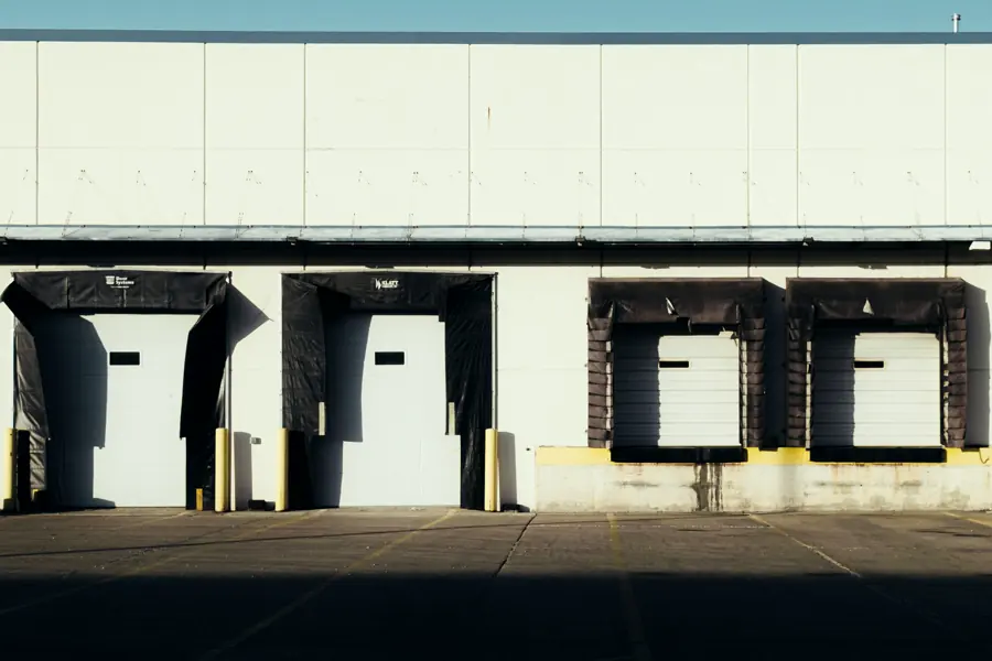 Four dock-high loading doors with black seals and yellow bollards along a pale warehouse wall.